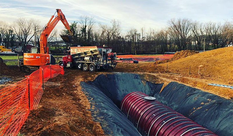 Excavator and truck backfilling a utility trench