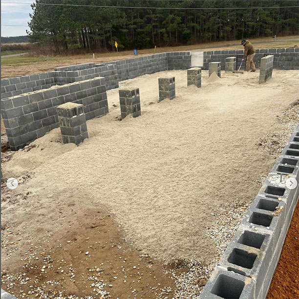 Worker placing structural fill inside block foundation walls